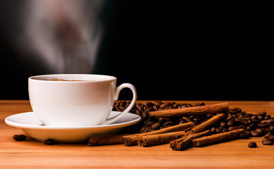 Coffee cup, coffee beans and cinnamon sticks on dark background