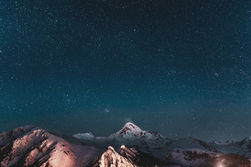 Obraz na płótnie Canvas Georgia. Winter Night Starry Sky With Glowing Stars Over Peak Of Mount Kazbek Covered With Snow. Beautiful Night Georgian Winter Landscape