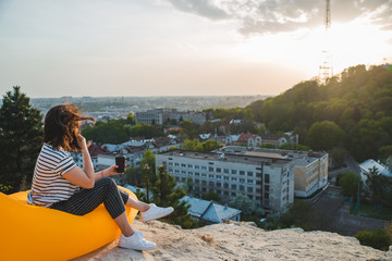 woman sitting on yellow inflatable mattress drinking coffee enjoying sunset over city