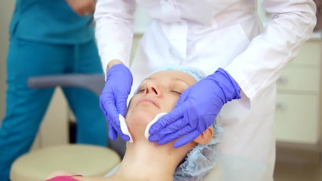 The concept of a beautician. cosmetologist applies lotion with cotton swab on woman face. skin cleansing