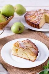 Piece of a pear cake on a white plate on a white table with pears
