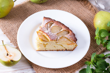 Piece of a pear cake on a white plate on a white table with pears
