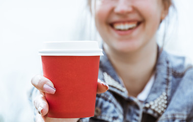 A girl holds a red paper cup of coffee. Glass of coffee close-up in hand.