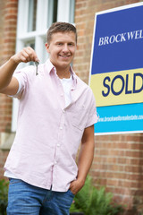 Portrait Of Excited Man Standing Outside New Home With Sold Sign Holding Keys