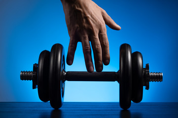 Male hand reaching for the dumbbell. Close-up. Blue background.