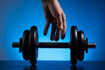 Male hand reaching for the dumbbell. Close-up. Blue background.