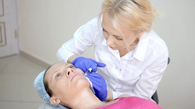 The cosmetologist makes injections, anti-aging procedures for tightening and smoothing wrinkles on the skin of the face and neck of a woman.