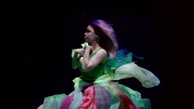 Portrait of a beautiful fairy girl with purple-green hair and purple lips, she has colored wings on her back, she is in a dress and in silks, floating under water on a dark background