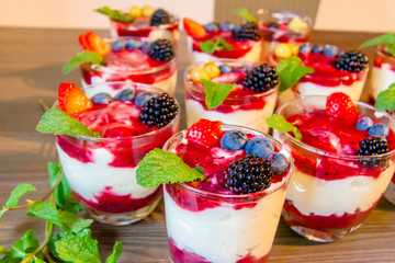 Eating yogurt with strawberry, blueberries, mint, granola, mulberry in a glass bowls, healthy food and plant-based food concept