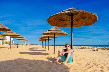 A teenage boy sitting under reed umbrella on the beach