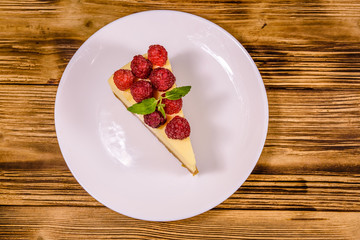 White plate with cheesecake New York, leaf of mint and raspberries on wooden table. Top view