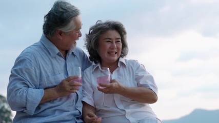 Asian couple senior drinking beverage together and emotion romantic summer on the beach. Concept of happy family, post retirement, celebration anniversary married, mental health and summer travel.