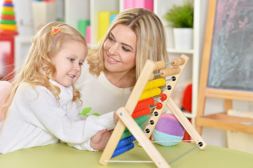 Portrait of mother with little daughter counting on abacus at home