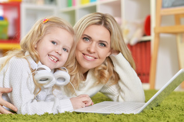 Portrait of mother with little daughter using laptop while lying on floor