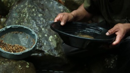Person looking for gold with a small gold pan at a little stream