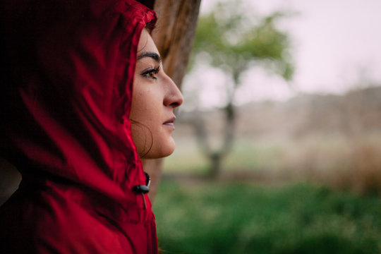 Girl wearing red raincoat observes the rain on the field