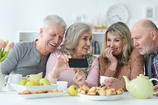 Two senior couples using smartphone during morning tea