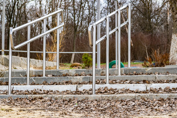 Modern embankment in the Rostov region, small railings and steps of gray concrete. Metal shiny stainless steel handles. The construction on nature, among trees in the usual clear day