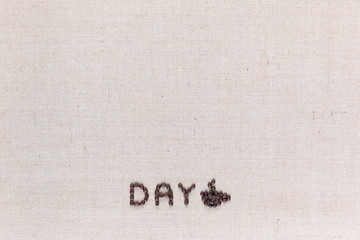 Day icon written with coffee beans with a cup on linen texture arranged bottom center.