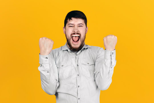 bearded man rejoices victory, clenching fists, image over orange  background