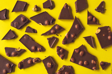 Broken chocolate bar with hazelnuts on yellow background, top view