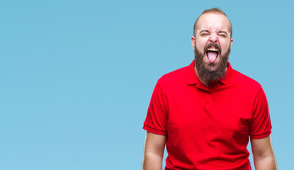 Young caucasian hipster man wearing red shirt over isolated background sticking tongue out happy with funny expression. Emotion concept.