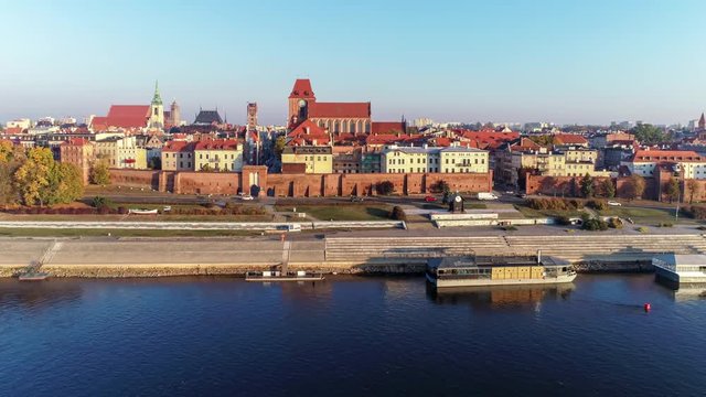Torun old city in Poland. Aerial revealing video in sunrise light with medieval Gothic St John Cathedral, town hall tower, Vistula river, historic buildings, town walls, gates and rowing boats
