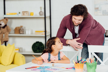 handsome father standing near cute daughter holding color pencil at home