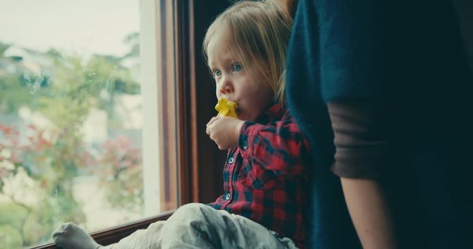 Little toddler by the window with mother eating ice lolly