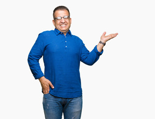 Middle age arab man wearing glasses over isolated background smiling cheerful presenting and pointing with palm of hand looking at the camera.