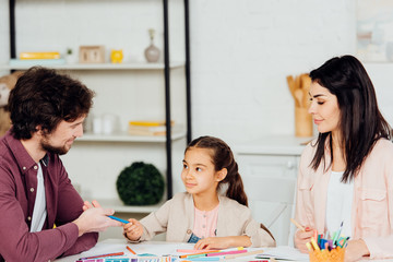 Fototapeta premium happy father giving felt pen to cute daughter near attractive wife