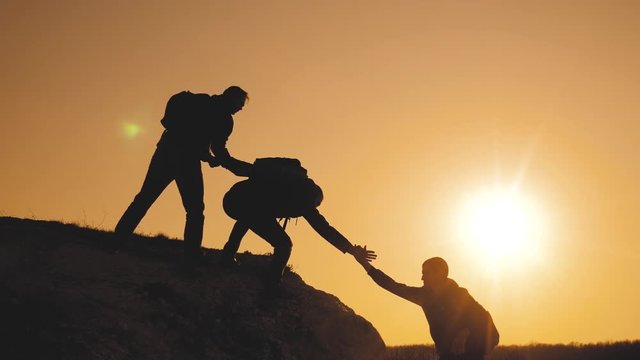 teamwork help business travel silhouette concept. group of tourists lifestyle lends a helping hand climb the cliffs mountains. people climbers climb to the top overcoming hardships the path to victory