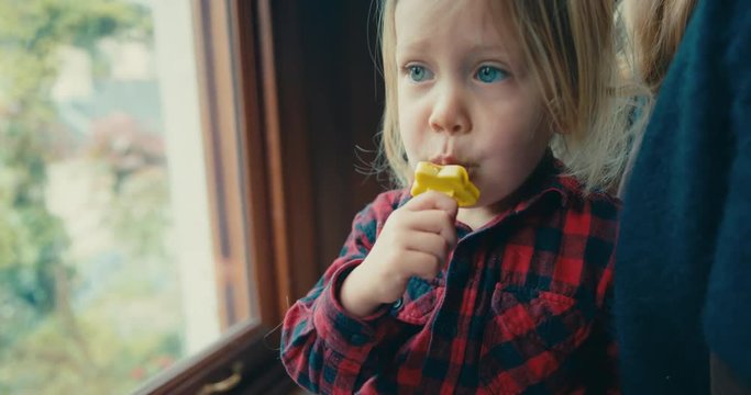 Little toddler eating an ice lolly by the window
