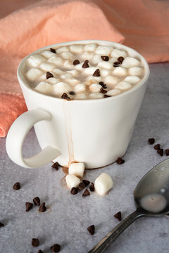 Hot cocoa in white cup dripping marshmallows next to coral napkin