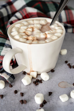 Hot chocolate spilling from white mug with marshmallows and spoon