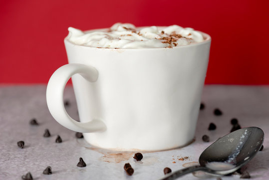 Closeup of creamy hot cocoa in white mug on red background