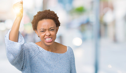 Young beautiful african american woman wearing a sweater over isolated background angry and mad raising fist frustrated and furious while shouting with anger. Rage and aggressive concept.