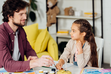 Fototapeta premium happy father looking at cute daughter holding paintbrush