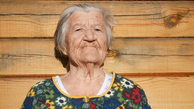 Grandma sadly looks into the camera.  Grandmother seriously thinks about something, looks into the camera, and then smiles slightly. 91 year old grandmother. She is wearing colored clothes.