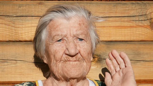 Granny is styling her hair.  Wrinkled face of aged woman. Grandmother on wooden rustic background touches her gray hair and gently puts it back. Old granny looks into the camera. 91 year old grandma.