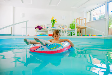 Summer holiday is comming. Happy little child girl playing in water with colorful child boat in swimming pool.