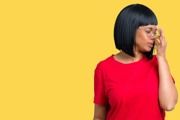 Beautiful young african american woman wearing glasses over isolated background smelling something...