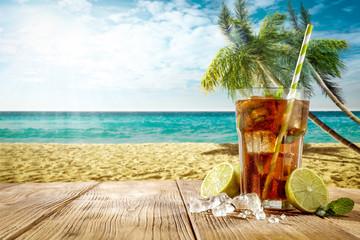 Cold summer drink on wooden table. Free space for your decoration. Beach landscape with ocean and palms. Summer sunny day. 