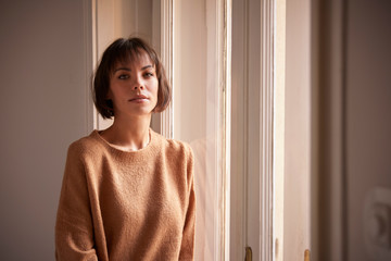 Beautiful smiling woman looking at camera while standing at the window