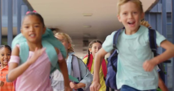 Front view of mixed-race schoolkids with schoolbags running in the corridor at school 4k