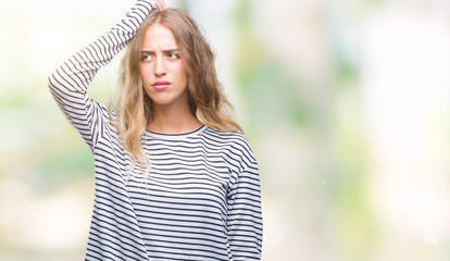 Beautiful young blonde woman wearing stripes sweater over isolated background confuse and wonder about question. Uncertain with doubt, thinking with hand on head. Pensive concept.