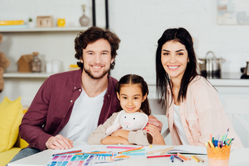 Fototapeta premium happy man and woman smiling with cute daughter holding soft toy and looking at camera