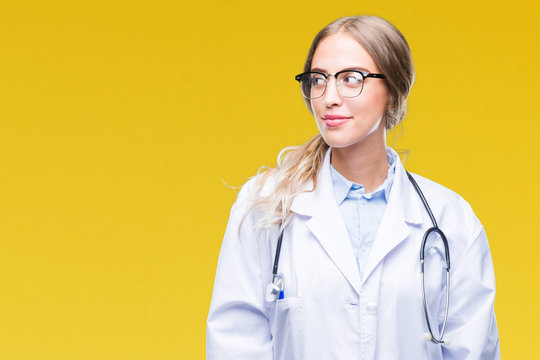 Beautiful young blonde doctor woman wearing medical uniform over isolated background smiling looking side and staring away thinking.