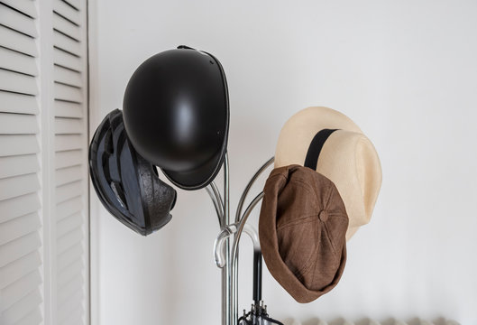 Perchero met&aacute;lico sobre el que est&aacute;n colgados sombrero Panam&aacute;, cascos bici, gorro y paraguas sobre un fondo de pared blanca