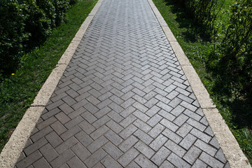 Paving slabs in the green garden. Texture of road tiles with herringbone pattern. Perspective view